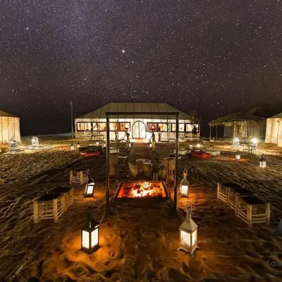 a building with a fire pit in the sand at night at Sahara Luxury Glamping in Merzouga