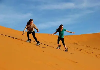 two women are skiing down a sand hill at Camel Experience Camp in Merzouga