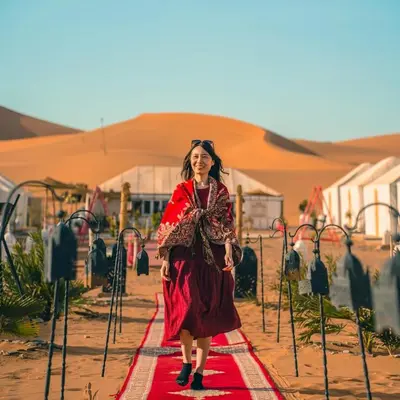 a woman in a red dress walking down a red carpet at Aisha Luxury Camp in Merzouga