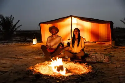 two people sitting next to a fire in front of a tent at Camp Desert Sky in Merzouga