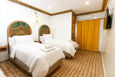 a bedroom with two beds with white sheets and yellow curtains at Dar Ibn Majdoub Prive Entier in Fès