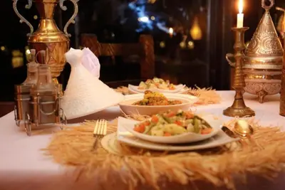 a table with plates of food on a table with a candle at Merzouga Sara Luxury Camp in Merzouga