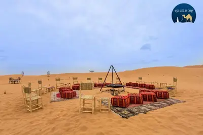 a desert with a table and chairs in the sand at Luxury Merzouga Camp in Merzouga