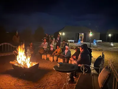 a group of people sitting around a fire at luna camp merzouga in Merzouga