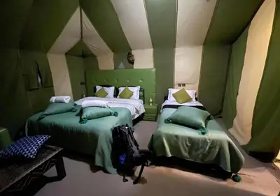 a green room with two beds and a table at Merzouga nights camp& excursions in Merzouga