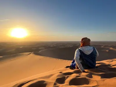 a woman sitting on a sand dune watching the sunset at Private Wild Tent Experience M'Hamid in Mhamid