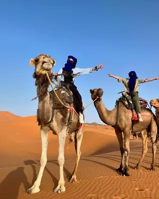 three people riding on the backs of camels in the desert at Soul Dunes Luxury Camp in Merzouga