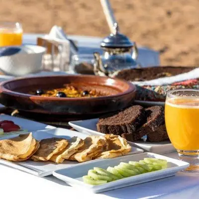 a table topped with plates of food and a bowl of food at Desert Bloom Luxury Camp in Merzouga
