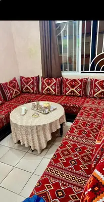 a living room with a red couch with a table at Aéroport Service navette vers logement cosy in Oulad Akkou