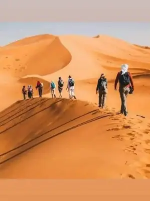 a group of people walking on a sand dune at Tasnim Désert Camp & Activités in Merzouga