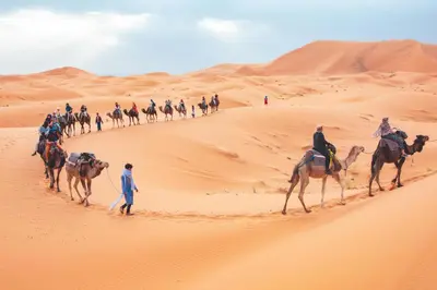 a group of people riding camels in the desert at Starlight Mirage Camp in Lac Yasmins