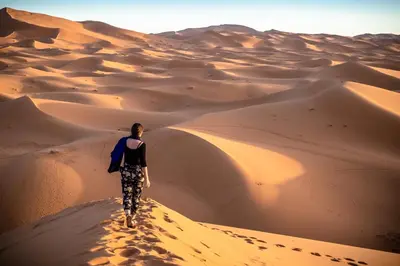 a woman walking on a sand dune in the desert at ERG merzouga desert Luxury camp in Merzouga