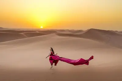 a woman in a dress running through the desert at Merzouga Eastern Camp Luxury in Merzouga