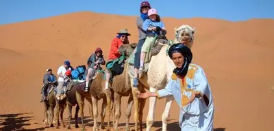 a group of people riding camels in the desert at TRIP Merzouga luxury camp in Hassilabied