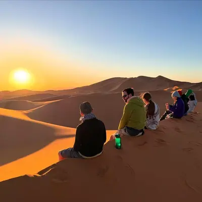 a group of people sitting in the desert watching the sunset at Sand Fish Camp in Merzouga