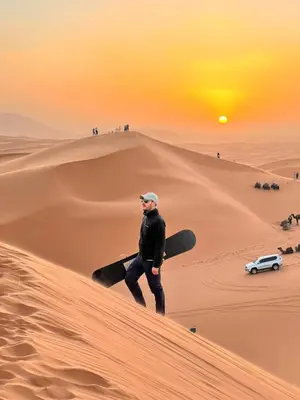 a man walking on a sand dune with a snowboard at Honeymoon Luxury Camp in Merzouga
