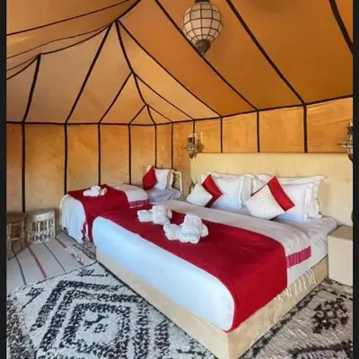 two beds in a tent with red and white pillows at Tilila Luxury Camp in Merzouga