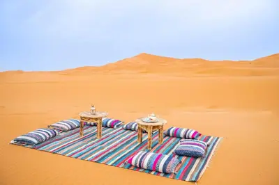 a blanket in the middle of a desert with two tables at sahara bliss camp in Merzouga