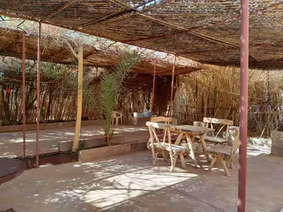 a patio with a table and chairs under a straw roof at Auberge chez hammadi