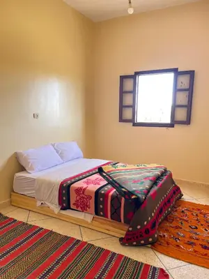 a bedroom with a bed and a window and a rug at Maison La Baraka Merzouga in Merzouga