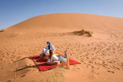 two people sitting on a blanket in the desert at Maps of dreams camp in Merzouga