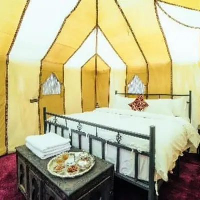 a bed in a tent with a plate of food on a table at Tenere Luxury Camp in Merzouga