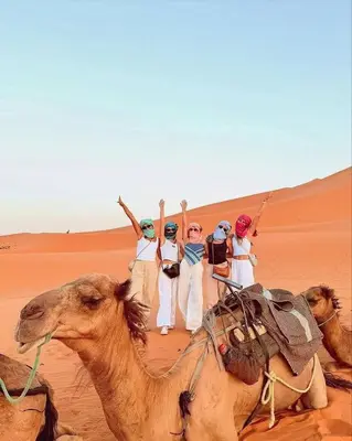 a group of people riding on the backs of camels in the desert at Merzouga luxury tente in Merzouga