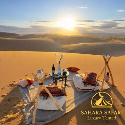 a table in the middle of a desert with the sunset at Sahara Safari Luxury Tented in Merzouga
