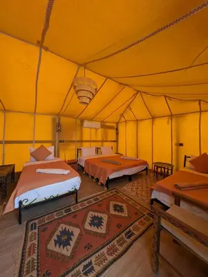 a large yellow tent with two beds in it at Berber Dreams Desert Camp in Merzouga
