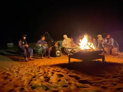 a group of people sitting around a fire at night at Aladdin Desert Camp - Mhamid Erg Chigaga Escape in El Gouera