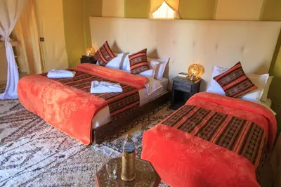a bedroom with two beds with red comforters at Sahara Desert Luxury Camp in Merzouga