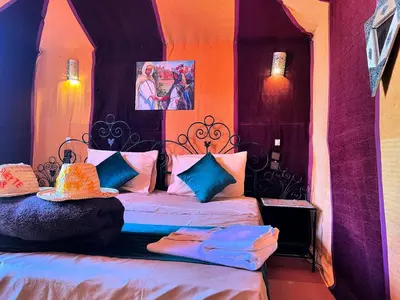 a bedroom with a bed with blue and pink pillows at Desert camp camel & sandboarding in Merzouga