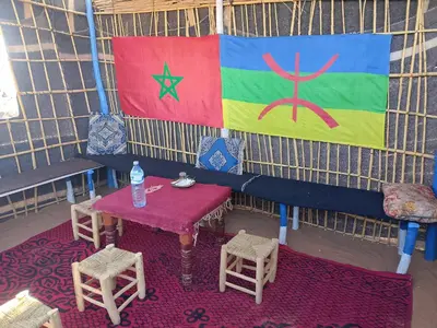 a tent with a table and chairs and a flag at Travel Oasis Merzouga Camp in Merzouga
