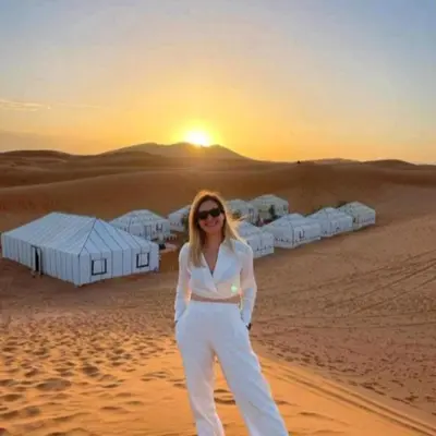 a woman standing in the desert at sunset at Merzouga Nice luxury Camp in Merzouga