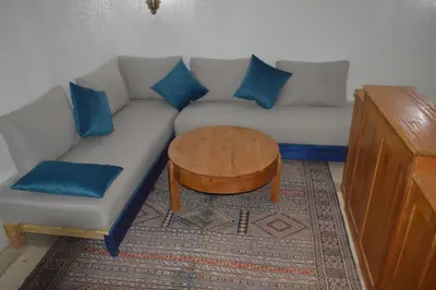 a living room with a couch with blue pillows and a table at Kasr Tin Hinane in Merzouga