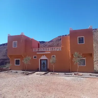 an orange building with trees in front of a mountain at Dar Brahim Resto Beds in Ouarzazate