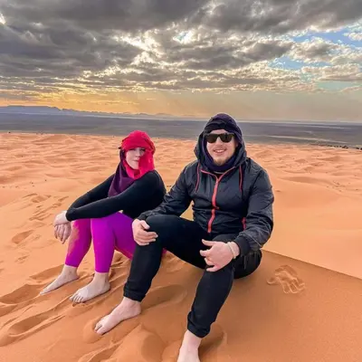 two people sitting on the sand in the desert at Authentic Desert Camp in Merzouga