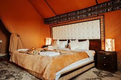 a bedroom with a large bed with an orange wall at Merzouga Sahara Camp in Merzouga